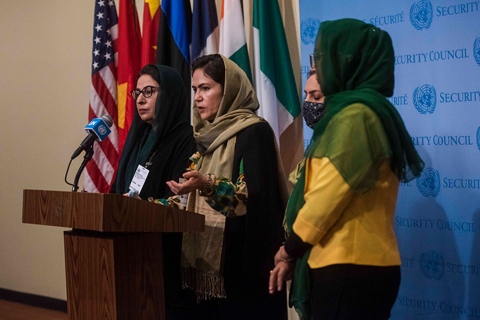 A woman gives a speech at the United Nations Security council. She is surrounded by three other women. Of the four women, three are hijabi. The fourth woman is wearing a mask.